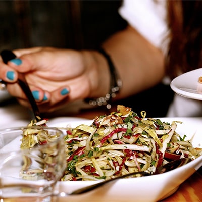 A woman holds a fork and spoon above a plate filled with food, preparing to enjoy her meal.