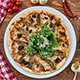 A delicious pizza topped with mushrooms, spinach, and assorted vegetables, elegantly presented on a white plate.