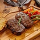  A succulent steak on a wooden cutting board, accompanied by fresh vegetables and slices of bread, ready to be served.