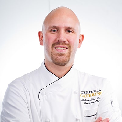 A smiling man wearing a chef's uniform, exuding warmth and professionalism in a culinary setting.