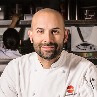 A smiling man wearing a chef's uniform, exuding warmth and professionalism in a culinary setting.
